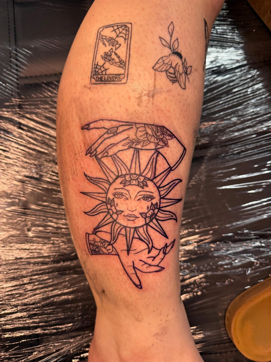 Illustrative sun tattoo with a hand on leg.