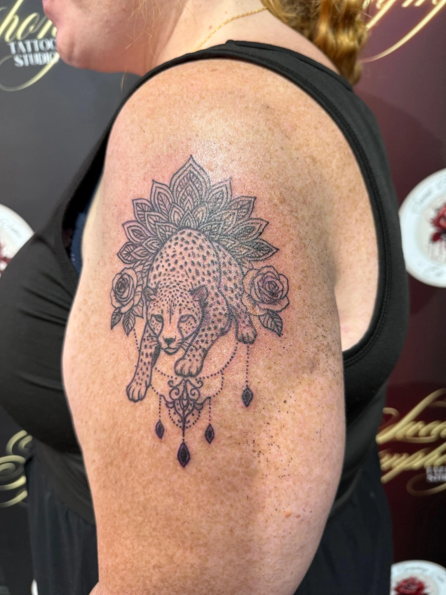 Illustrative leopard tattoo with mandala and roses on shoulder.