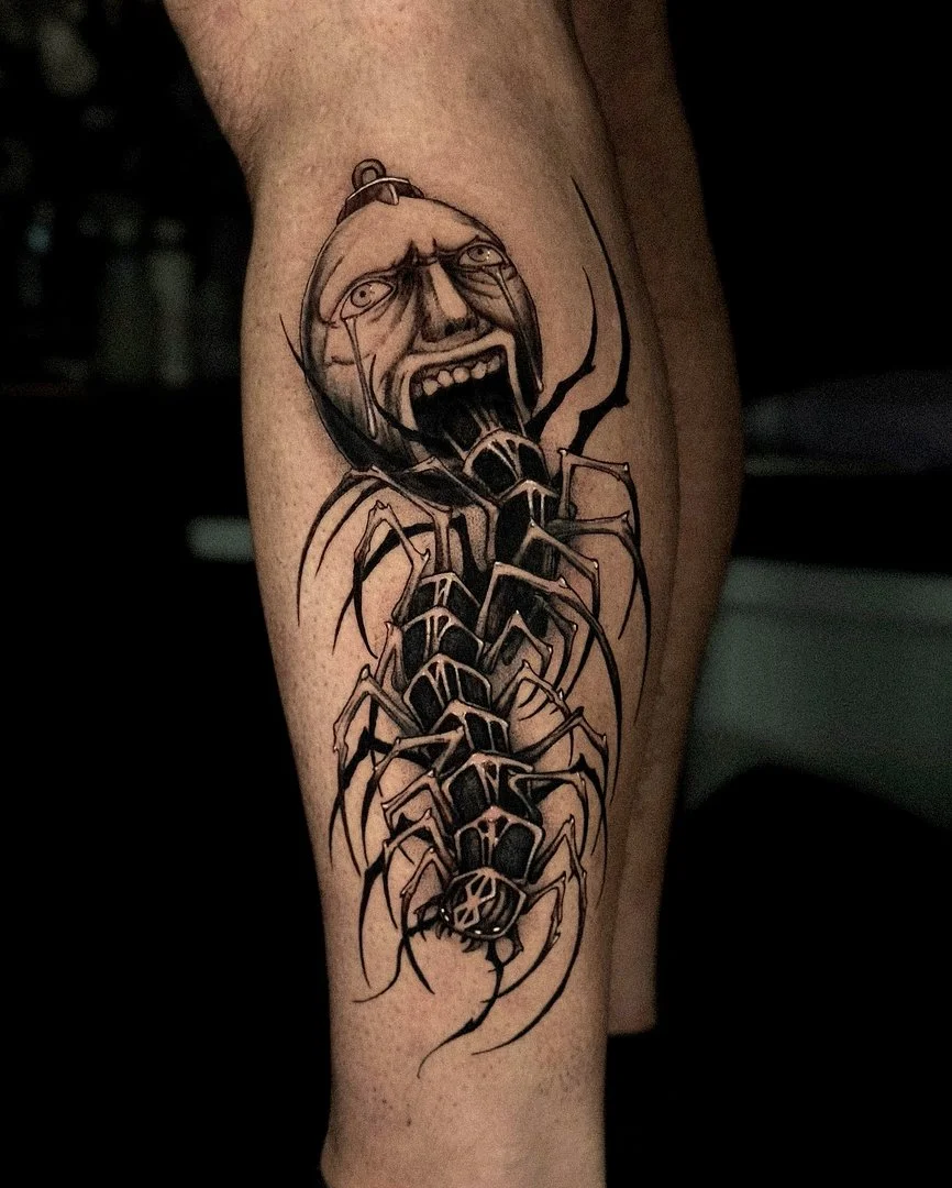Black-and-grey scorpion tattoo with a face on leg.