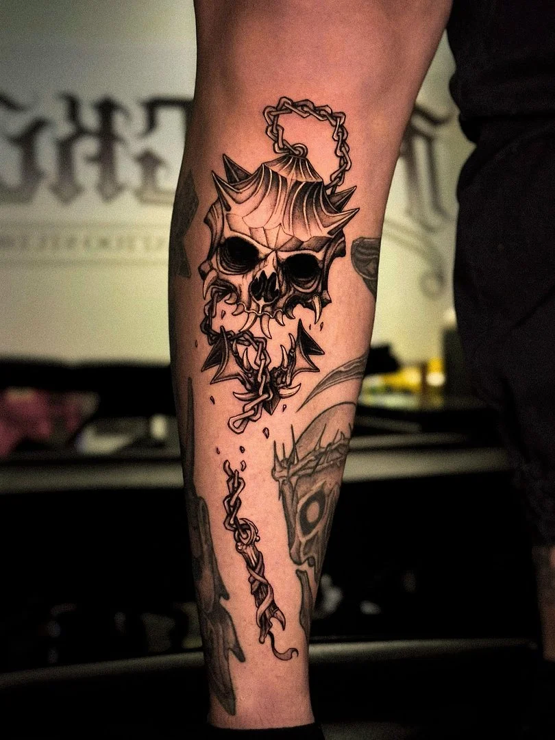Detailed skull tattoo with spider web and chains on leg.