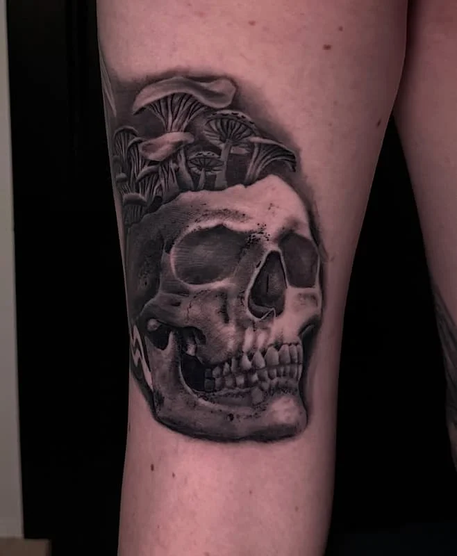 Black-and-grey skull tattoo with mushrooms on thigh.