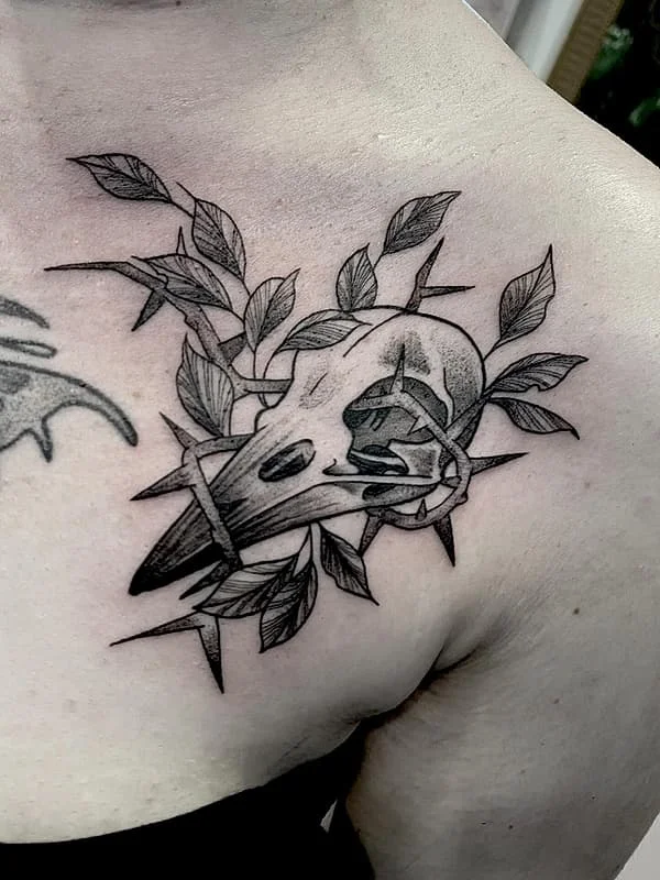 Black-and-grey skull tattoo with leaves and thorns on chest.