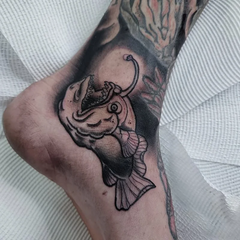 Realistic black-and-grey fish tattoo on ankle.