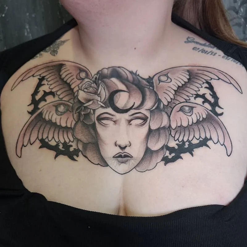Black-and-grey angel tattoo with wings and rose on chest.
