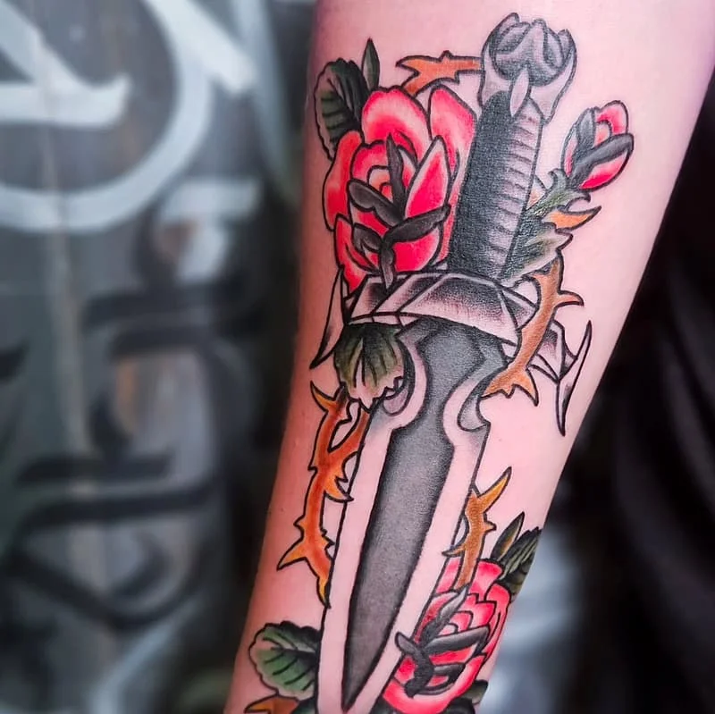 Traditional tattoo of a dagger with roses on forearm.