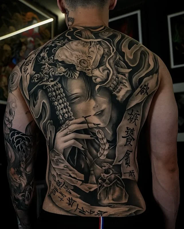 Large black-and-grey Japanese tattoo on back featuring a woman's face and skull.