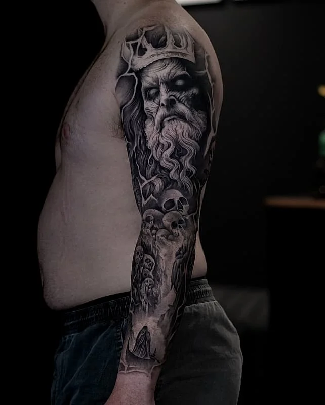 Black-and-grey full-sleeve tattoo of a mythical figure with skulls.