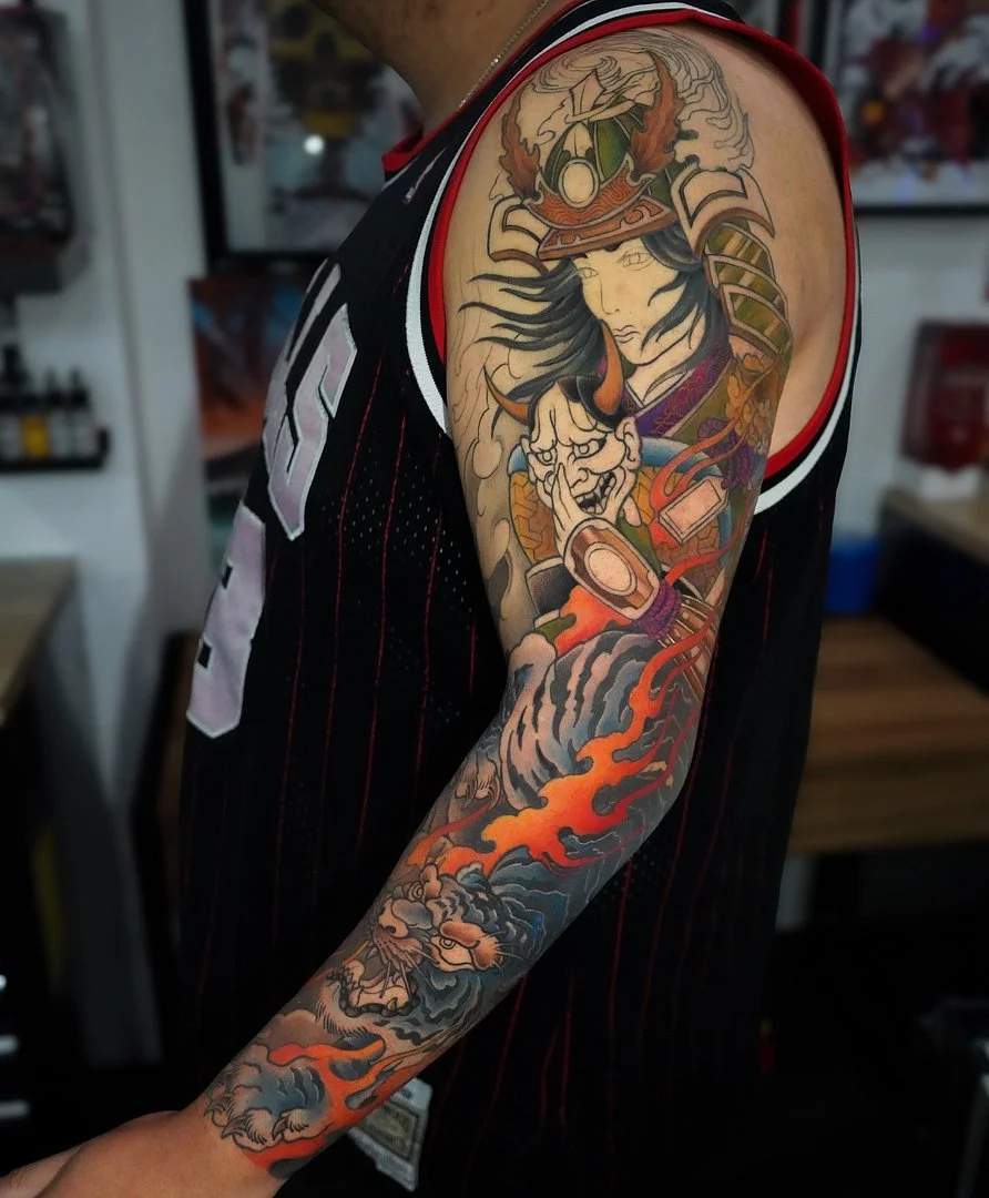 Full-sleeve tattoo of a samurai and dragon with flames.