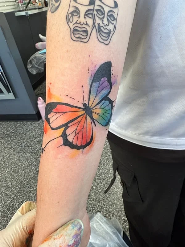 Colorful watercolor butterfly tattoo on forearm.