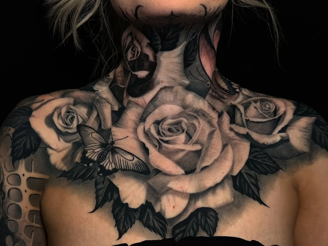 Realistic black-and-grey roses and butterfly tattoo on chest and neck.