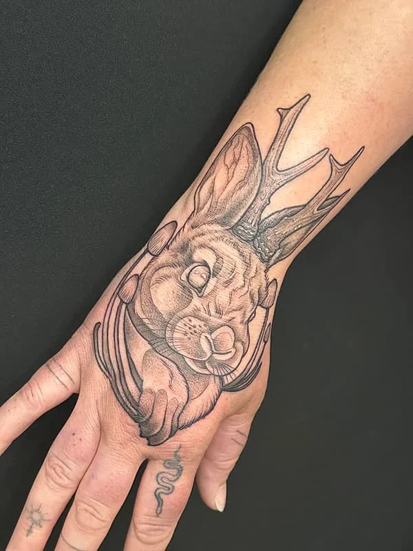 Illustrative rabbit tattoo with antlers on hand.
