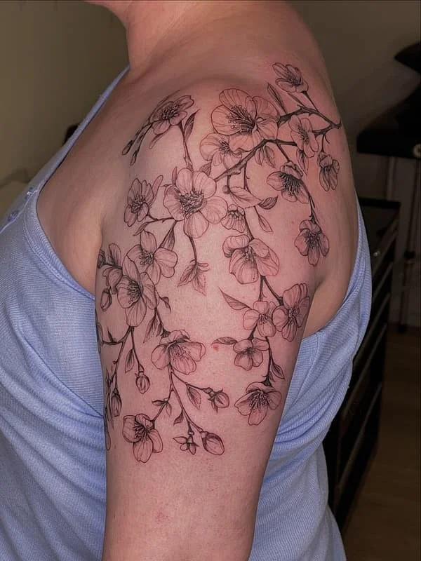 Fine-line cherry blossom tattoo on shoulder and arm.