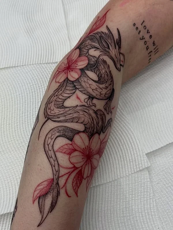 Illustrative dragon tattoo with flowers on forearm.