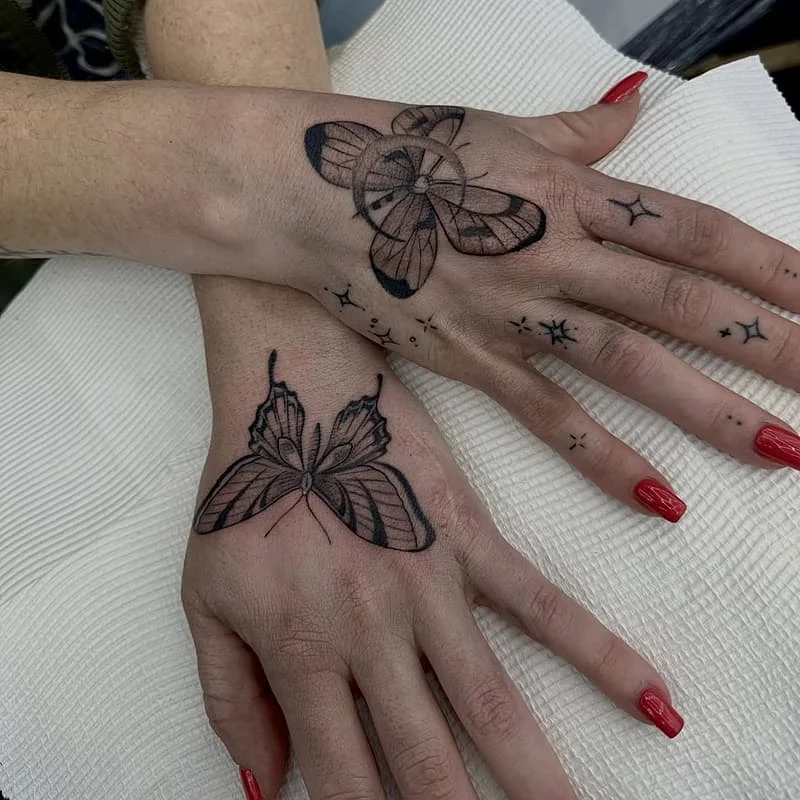 Intricate blackwork butterfly tattoos on hands.