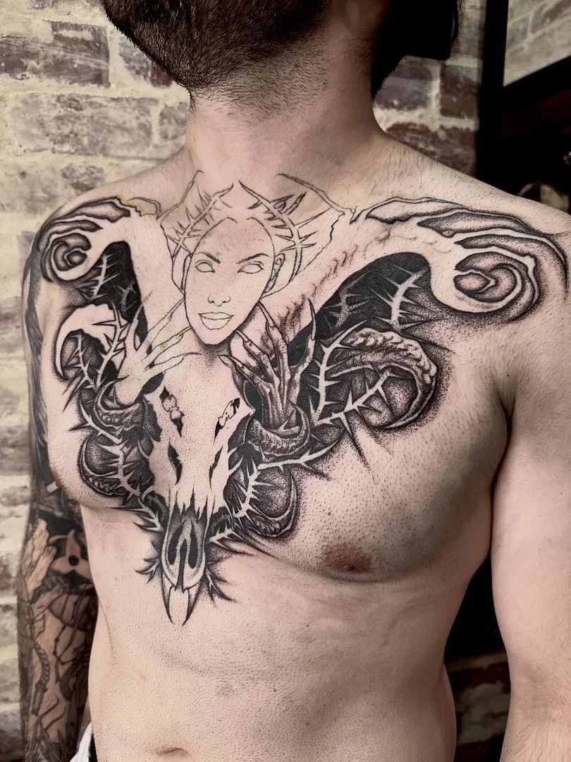 Large black and grey chest and shoulder tattoo featuring a skull and figure