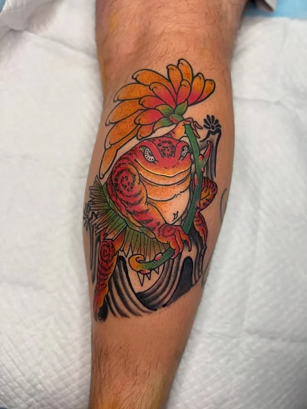 Colorful frog tattoo with flowers on leg.