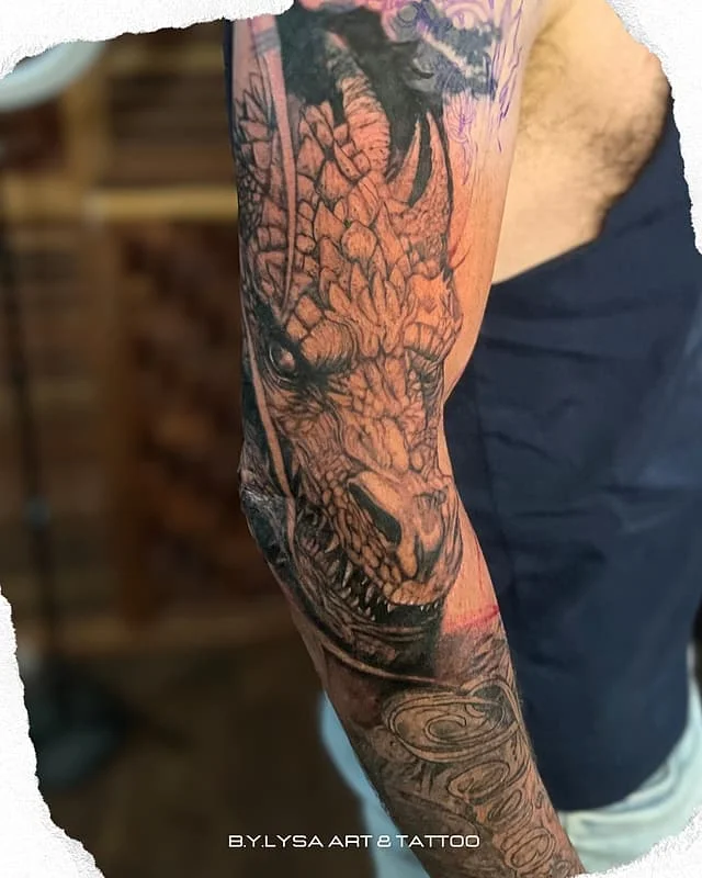 Detailed black-and-grey dragon tattoo on arm.