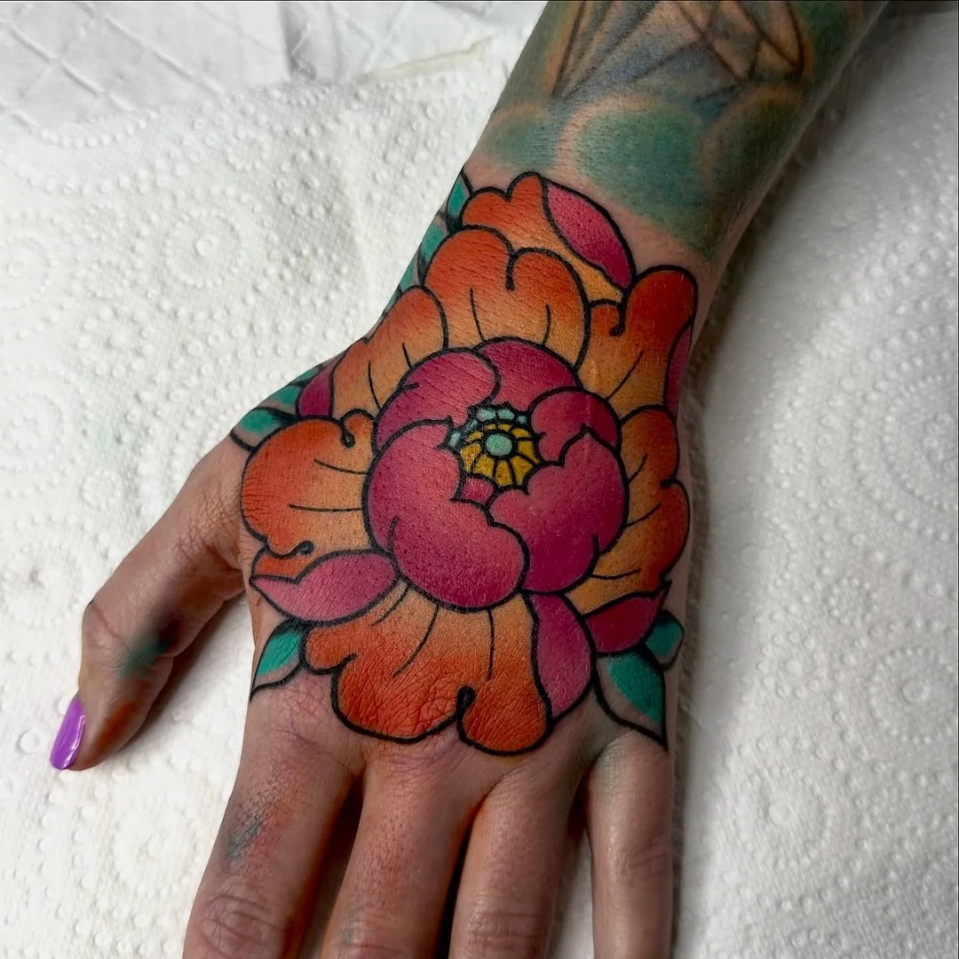 Vibrant peony tattoo on a hand.