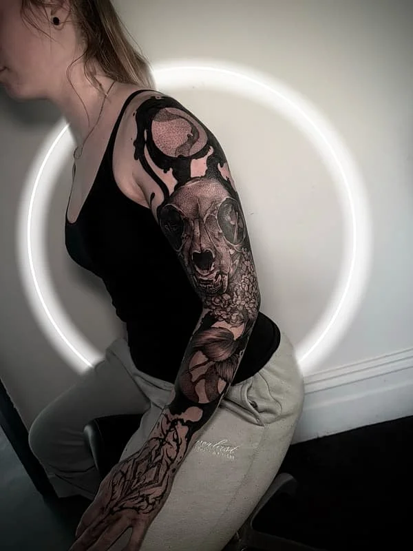Detailed black-and-grey full-sleeve tattoo featuring an animal skull.