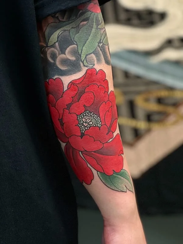 Vibrant red peony tattoo on the arm.