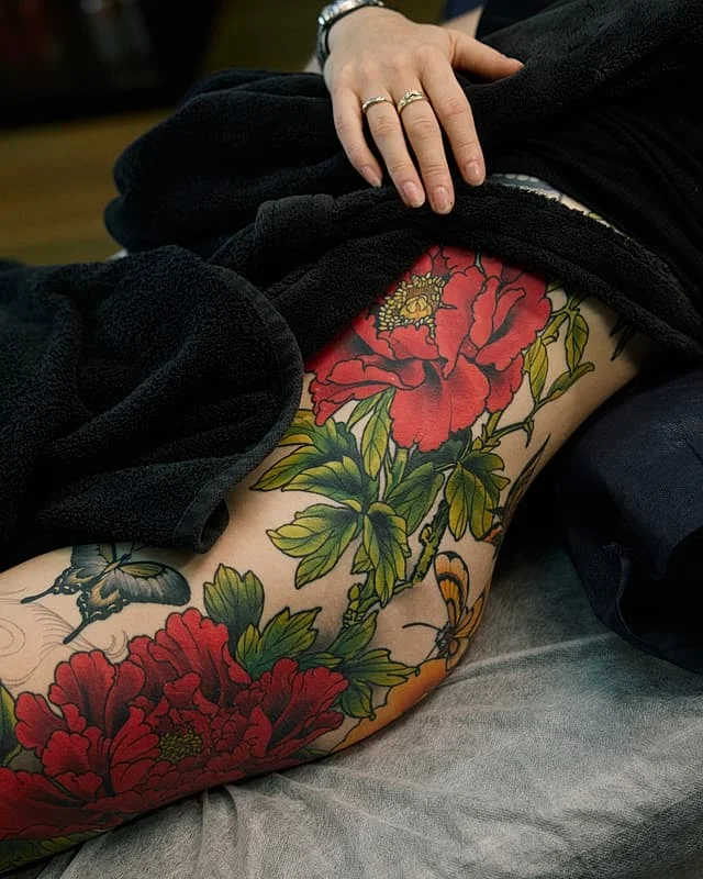 Vibrant watercolor tattoo of flowers and butterflies on thigh.