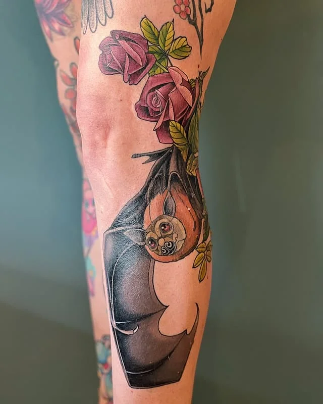 Illustrative tattoo of a bat and roses on a leg.