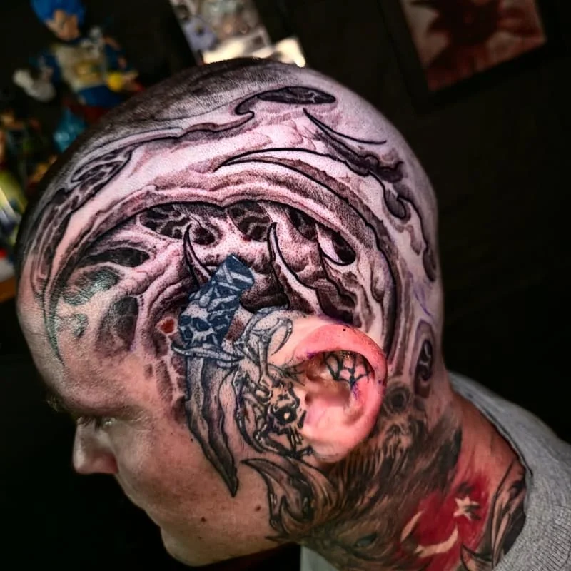 Intricate black-and-grey tattoo on the head featuring waves and a dragon.
