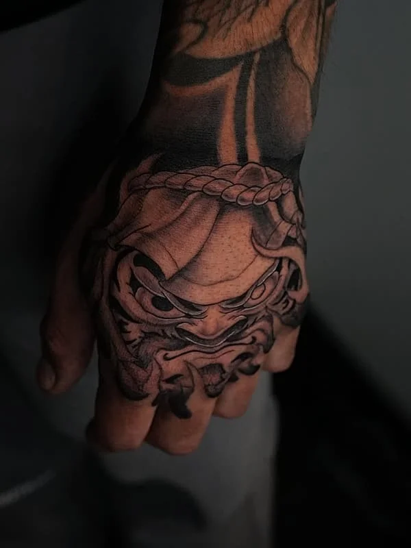 Black-and-grey samurai mask tattoo on hand.