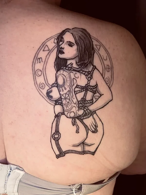 Illustrative blackwork tattoo of a woman on shoulder.