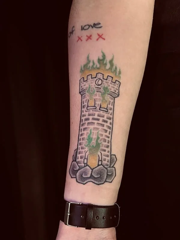 Colorful castle tattoo with flames on forearm.
