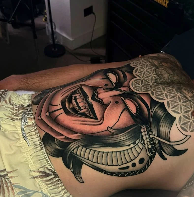 Large black-and-grey tattoo of a mask on the back.