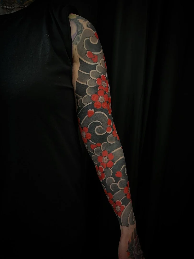 Full-sleeve tattoo with cherry blossoms and wave patterns.