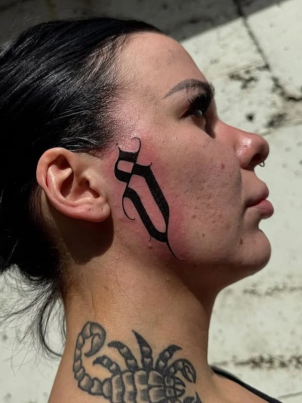 Minimalist black script tattoo on the side of a woman's face.