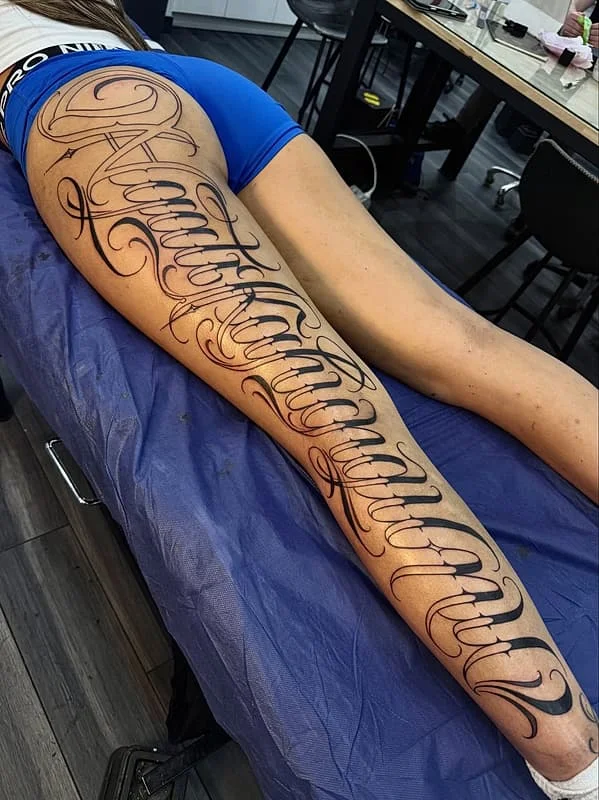 Large elegant script tattoo on a woman's leg.