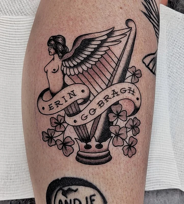 Black-and-grey tattoo of a winged woman and harp on arm.