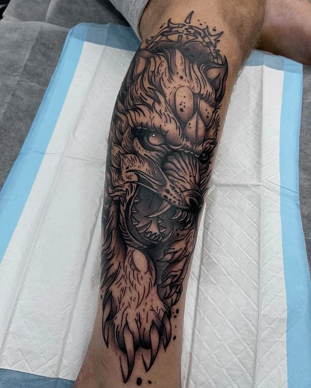Realistic black-and-grey wolf tattoo on calf.