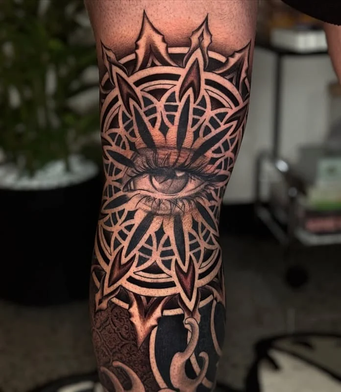 Large black and grey geometric eye tattoo on leg.
