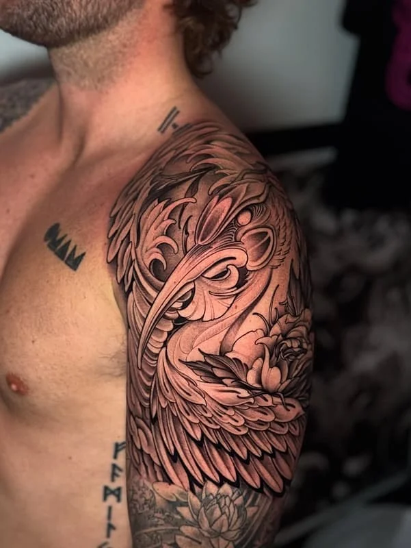 Large black-and-grey tattoo of a bird and rose on arm.