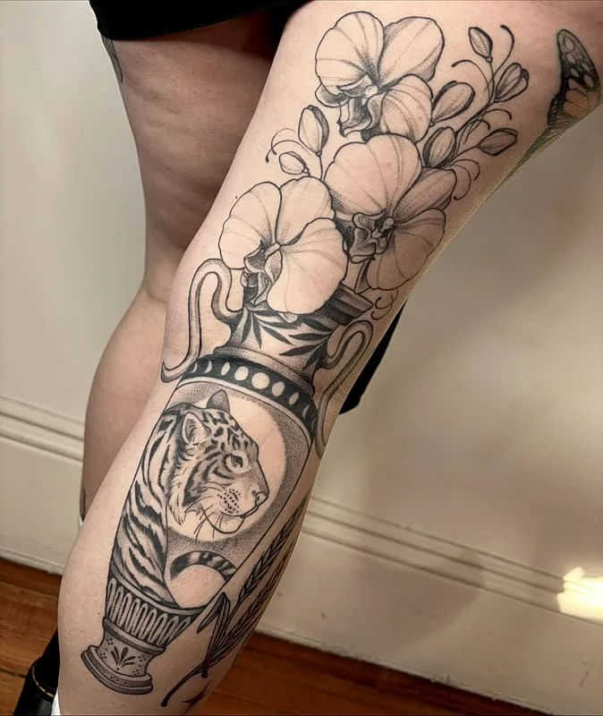 Black and grey tattoo of a tiger and orchids on leg.