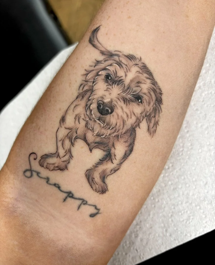 Realistic dog tattoo on forearm with script lettering.