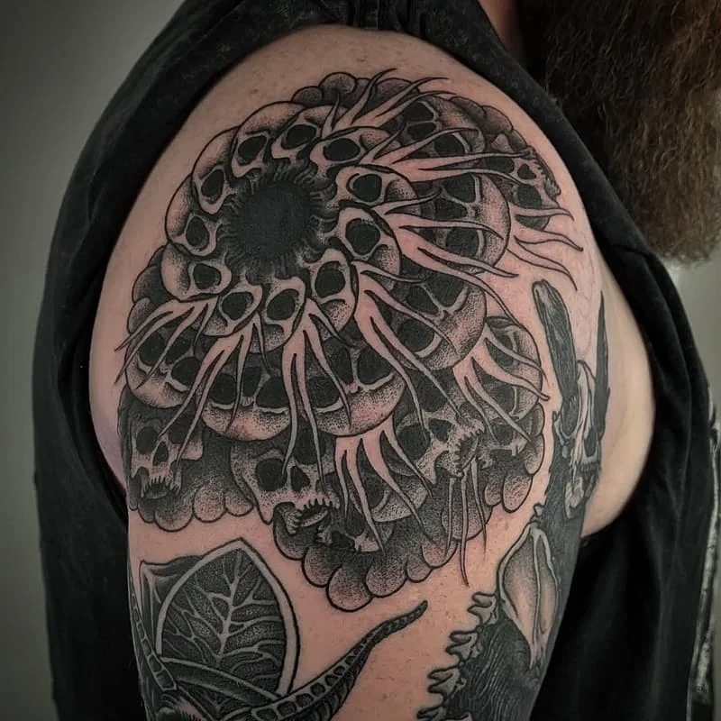 Large black-and-grey tattoo of skulls on shoulder.