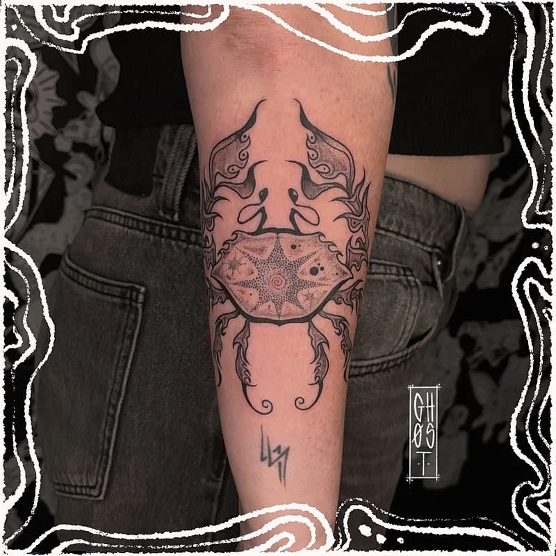 Blackwork crab tattoo on forearm with geometric elements.