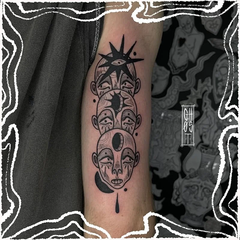 Abstract blackwork tattoo on forearm featuring faces and symbols.