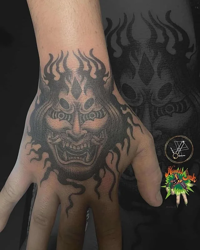 Detailed blackwork tattoo of a demon face on hand.