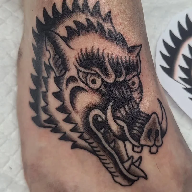 Blackwork tattoo of an aggressive boar on ankle.