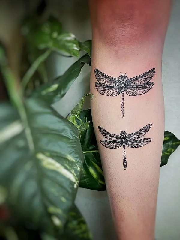 Fine-line dragonfly tattoos on a calf.