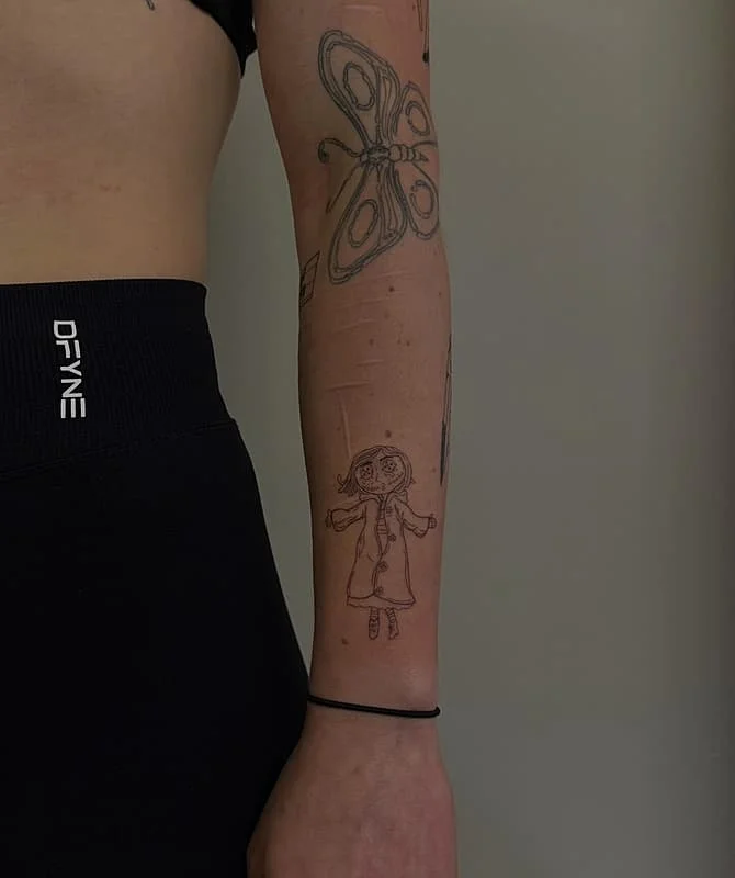 Whimsical fine-line tattoo of a cartoon girl on forearm.