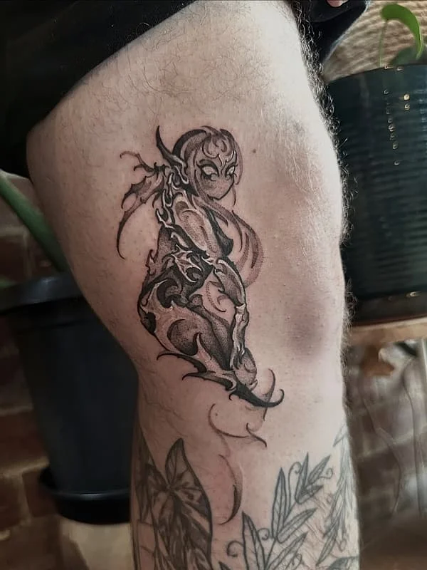 Black-and-grey illustrative tattoo of a female figure on thigh.