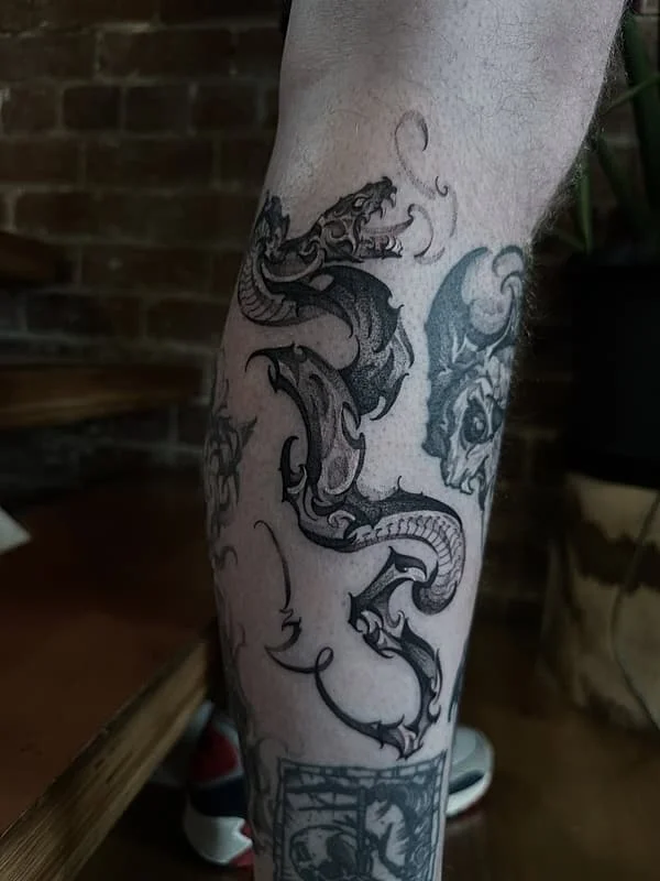 Intricate black-and-grey dragon tattoo on calf.