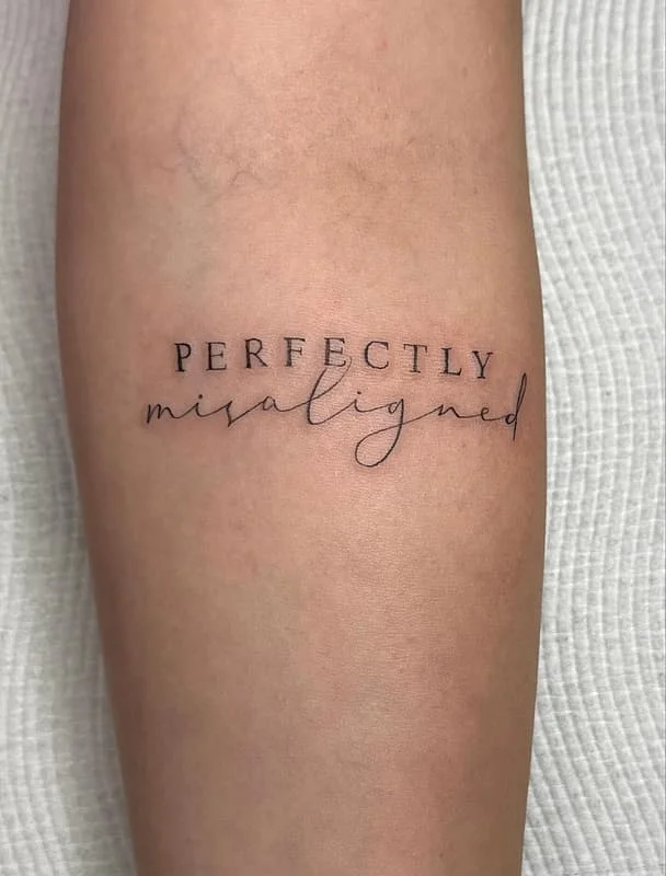 Minimalist script tattoo on forearm reading perfectly misaligned